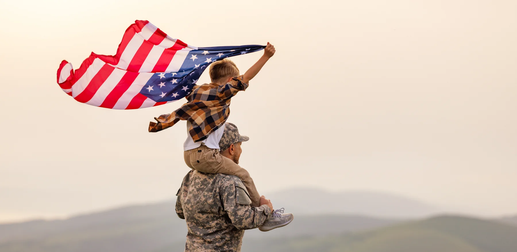 A U.S. service member carrying a child holding an American flag
